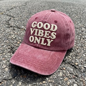 Op de afbeelding: Een vervaagde kastanjebruine honkbalpet met de tekst GOOD VIBES ONLY geborduurd in cr&egrave;mekleurige, verhoogde letters op de voorpanelen. De pet heeft een gebogen klep met zichtbare stiksels en een knoop op de bovenkant van de kroon.