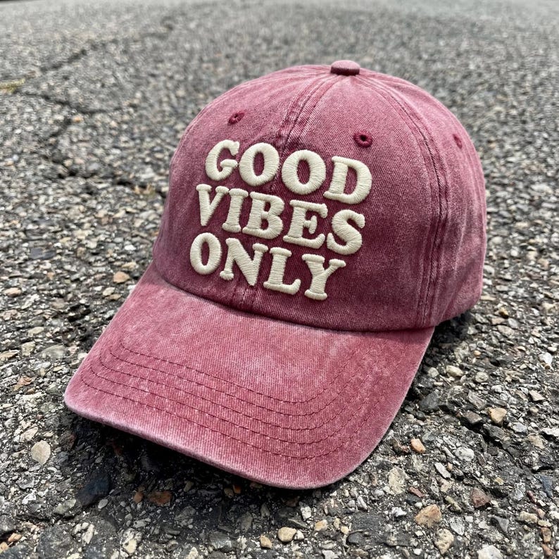 Op de afbeelding: Een vervaagde kastanjebruine honkbalpet met de tekst GOOD VIBES ONLY geborduurd in cr&egrave;mekleurige, verhoogde letters op de voorpanelen. De pet heeft een gebogen klep met zichtbare stiksels en een knoop op de bovenkant van de kroon.