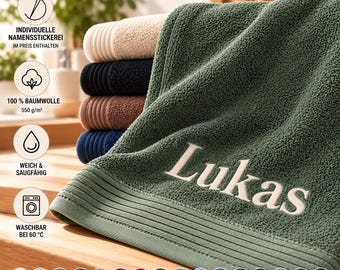 Könnte beinhalten: Ein Stapel gefalteter Baumwollhandtücher in verschiedenen Farben wie Beige, Schwarz, Braun, Blau und ein olivgrünes Handtuch obenauf mit dem eingestickten Namen Lukas in weißer Schreibschrift und einer gerippten Bordüre.