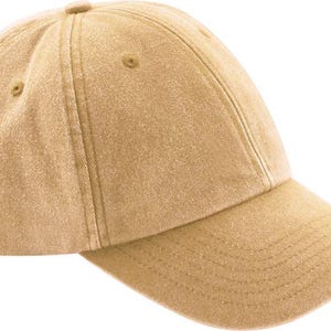 Op de afbeelding: Een effen beige baseballpet met een constructie van zes panelen, voorzien van een gebogen klep, gestikte oogjes op elk paneel en een knoop aan de bovenzijde. De stof heeft een zachte, licht verweerde textuur in een egale kleur.