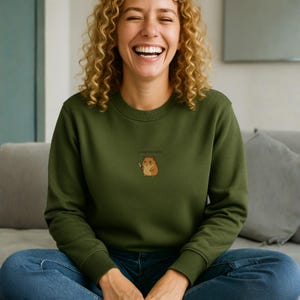 May include: An olive green sweatshirt with a cartoon hamster holding a knife, and the text "I'm a little snack" above the graphic. The sweatshirt is made of a soft material.