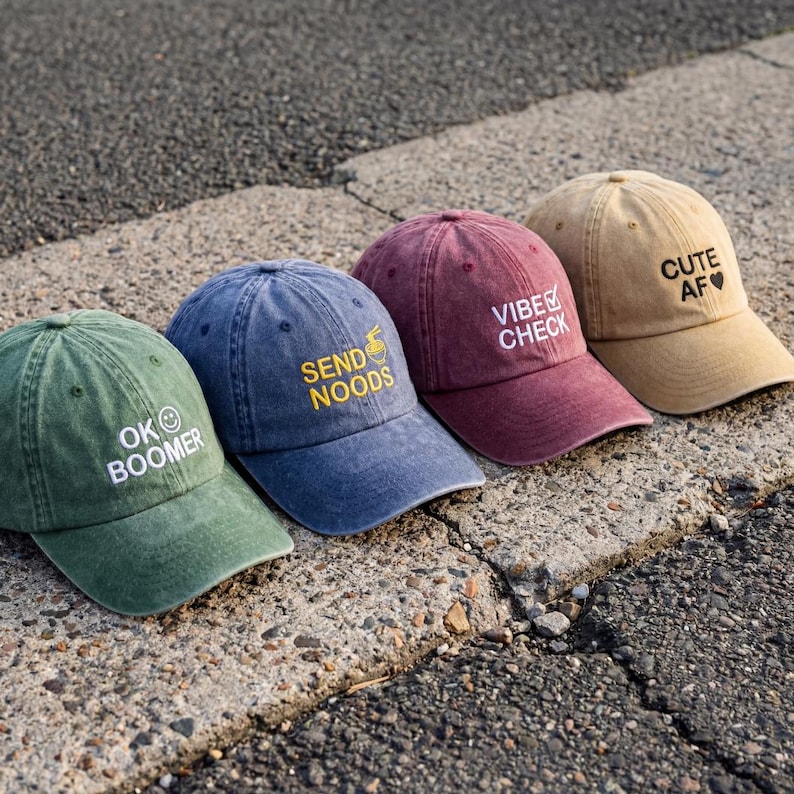Op de afbeelding: Vier baseballpetten in groen, blauw, bordeaux en beige. De groene pet heeft de tekst OK BOOMER met een smiley. De blauwe pet heeft de tekst SEND NOODS met een noedelkom-icoon. De bordeaux pet heeft de tekst VIBE CHECK met een vinkje. De beige pet heeft de tekst CUTE AF met een hartje.