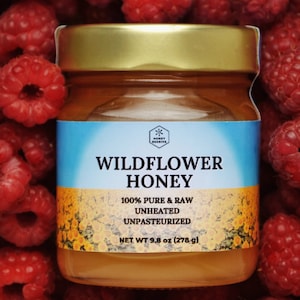 Peut inclure: Un pot en verre de miel de fleurs sauvages avec un couvercle doré. Le pot est entouré de framboises rouges. L'étiquette indique "Miel de fleurs sauvages", "100% pur et brut", "Non chauffé", "Non pasteurisé" et "Poids net 9,8 oz (278 g)".