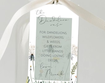 May include: A clear glass vase holds yellow dandelions and white dandelions. A white ribbon is tied around the neck of the vase. A tag with text is attached to the vase. The tag reads "the Dandelion vase" and other text.