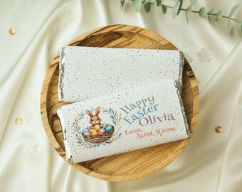 May include: Two white chocolate bars wrapped in foil with a silver glitter design. The top bar has a bunny rabbit holding colorful Easter eggs in a basket. The bottom bar has the text "Happy Easter Olivia Love, Aunt Renee".