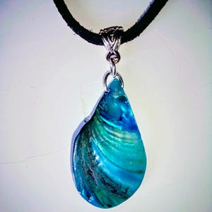 May include: A teardrop-shaped pendant necklace with a vibrant blue and green shell design. The pendant is suspended from a black cord necklace with a silver-colored clasp. The shell has a glossy finish and displays a range of blues and greens.