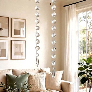 May include: A ceiling fan with five wooden blades and a central light fixture, featuring two long pull chains decorated with clear, faceted crystal beads and ending in a pointed crystal drop, hanging vertically from the fan housing.