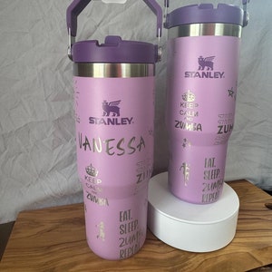 May include: Two light purple Stanley travel mugs with silver accents and handles. One mug has the name "Vanessa" and the words "Keep Calm and Zumba" printed on it. The other has "Eat, Sleep, Zumba, Repeat" printed on it.
