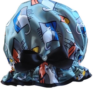 May include: A blue shower cap with a white satin lining and a black bow. The cap is decorated with a repeating pattern of white cats in geometric shapes.