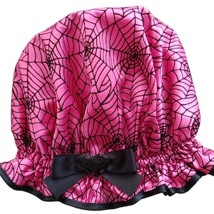 May include: Pink satin shower cap with a black spiderweb pattern and a black bow with a sparkly heart in the center.