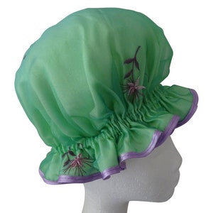 Peut inclure: Une charlotte de douche en satin vert avec une bordure violette et une broderie florale.