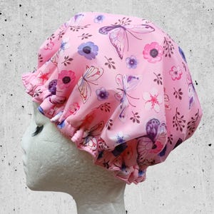 May include: Pink shower cap with a floral and butterfly print. The cap is made of a soft, waterproof material and has an elastic band to fit most head sizes.