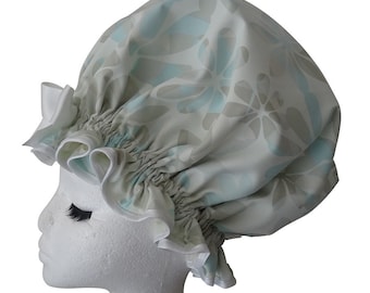 May include: A shower cap with a floral pattern in shades of blue, gray, and white. The cap has a gathered design and a white ruffled trim. The cap is designed to protect hair from water while showering.