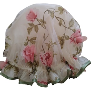 May include: A white shower cap with a floral print featuring pink roses and green leaves. The cap has a ruffled edge with a green trim.