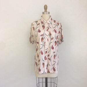 May include: A short-sleeved button-down shirt with a floral print in shades of orange, red, and blue on a cream background.