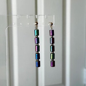 May include: A pair of long, iridescent earrings with a silver tone. Each earring features six rectangular beads in shades of green, purple, and blue.