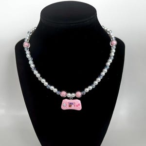 May include: A pink and white beaded necklace with a pink handheld game console charm.