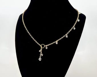 May include: A gold chain necklace with a small circle pendant and clear crystal accents dangling from the chain.
