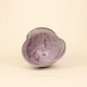 May include: A handcrafted ceramic bowl with a unique, organic shape. The bowl features a speckled, deep purple interior and a gray exterior. The rim has a wavy design, adding to its artistic appeal. This decorative bowl is suitable for serving or display.
