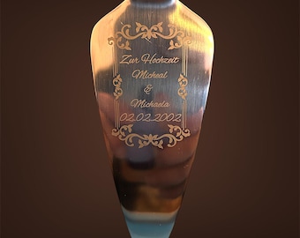 May include: A silver cake server with an ornate design and the text "Zur Hochzeit Micheal & Michaela 02.02.2002". The server has a decorative handle and is reflected in the surface below. The text "Langweider Geschenkelädle" is at the top.