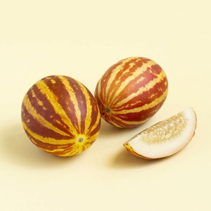 Puede incluir: Dos melones enteros rayados de amarillo y rojo y una rebanada del mismo melón con pulpa blanca y semillas negras.
