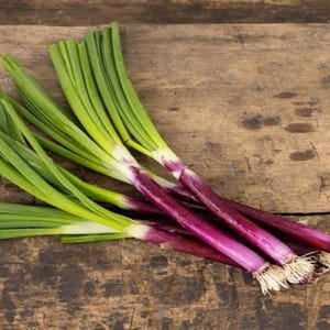 Könnte beinhalten: Ein Bund frischer grüner Schalotten mit violetten Zwiebeln. Die Schalotten liegen auf einer rustikalen Holzoberfläche.