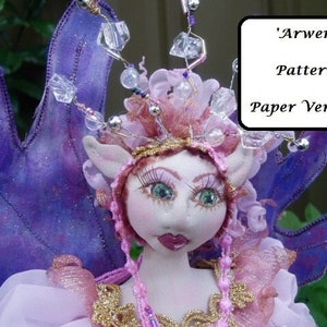 May include: A handcrafted fairy doll with large purple wings and a delicate face. The doll has a pink and gold bodice, a jeweled headpiece, and the text "'Arwen' Pattern Paper Version" in a white box.