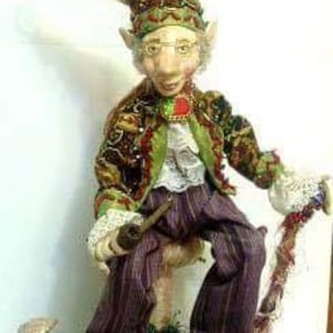 Puede incluir: Una muñeca artesanal de estilo caprichoso con una chaqueta estampada en verde y marrón, pantalones a rayas morados y blancos y un sombrero puntiagudo. La muñeca sostiene una pipa y está sentada en un hongo.