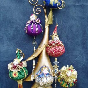 May include: A set of six handmade Christmas ornaments featuring whimsical jester figures with colorful fabric and bead embellishments. The ornaments are hanging from a gold metal stand.