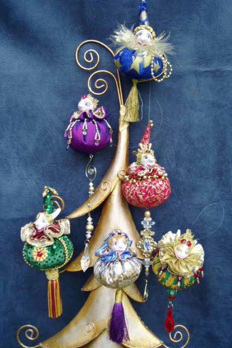 May include: A set of six handmade Christmas ornaments featuring whimsical jester figures with colorful fabric and bead embellishments. The ornaments are hanging from a gold metal stand.