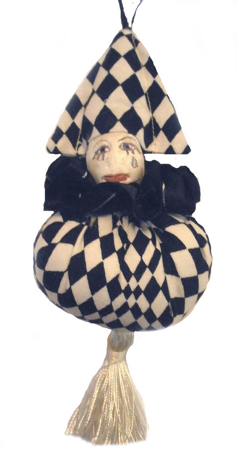 May include: A black and white checkered fabric jester doll with a white tassel. The doll has a painted face with tear drops and a red mouth.