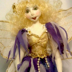May include: A handmade doll with blonde curly hair, wearing a purple and gold dress with a pearl necklace and white wings.
