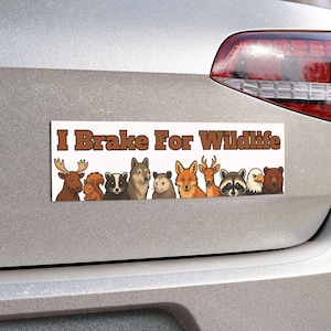May include: A white bumper sticker with the text "I Brake For Wildlife" in brown letters. Below the text are cartoon illustrations of various animals, including a deer, squirrel, wolf, fox, raccoon, and bear.