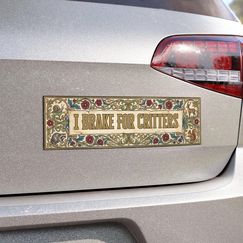 May include: Rectangular car magnet with the text "I Brake for Critters" in a decorative font. The magnet features a cream-colored background with floral and animal illustrations, including a raccoon, deer, and squirrel, and red and blue accents.