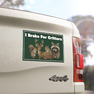 May include: A rectangular bumper sticker with the text "I Brake For Critters" above an illustration of a squirrel, deer, turtle, and raccoon on a green background. The sticker is affixed to the back of a white vehicle.