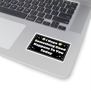 Pu&ograve; includere: Un adesivo rettangolare con sfondo nero e bordo bianco. L'adesivo presenta il testo "I Hope Something Good Happens To You Today" in bianco. Il design include piccole stelle bianche e margherite gialle.