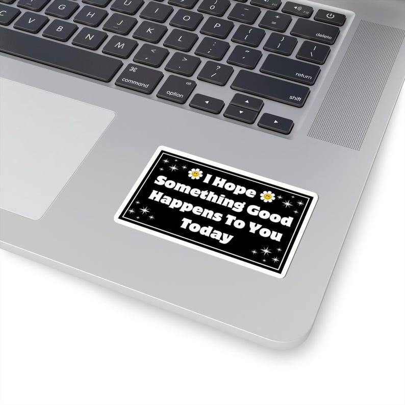 Pu&ograve; includere: Un adesivo rettangolare con sfondo nero e bordo bianco. L'adesivo presenta il testo "I Hope Something Good Happens To You Today" in bianco. Il design include piccole stelle bianche e margherite gialle.