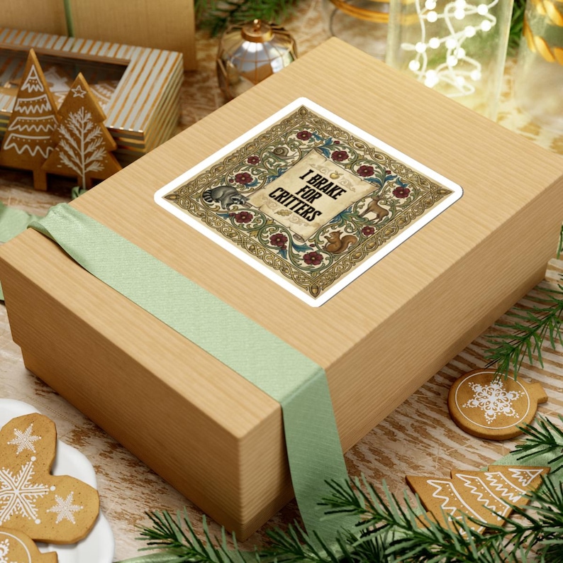 May include: A square sticker with the text "I Brake for Critters" in a decorative frame featuring a raccoon and squirrel. The sticker is on a light brown box with a green ribbon, surrounded by holiday decorations.