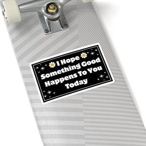 Pu&ograve; includere: Un adesivo rettangolare con sfondo nero e bordo bianco. L'adesivo riporta la scritta "I Hope Something Good Happens To You Today" in bianco. L'adesivo &egrave; decorato con fiori gialli e stelle.