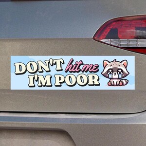 May include: A rectangular bumper sticker with the text "DON'T hit me I'M POOR" in white and pink lettering on a light blue background. A cartoon raccoon with teary eyes is on the right side of the sticker.