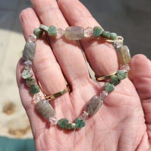 Op de afbeelding: Een groene en grijze edelsteen armband met heldere kristallen kralen. De armband is gemaakt van natuurlijke stenen en is een prachtig sieraad.