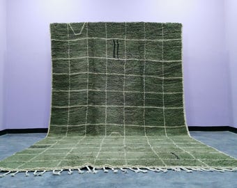 May include: A large, rectangular green rug with a grid pattern of white lines. The rug has a thick, textured pile and a fringe along the bottom edge. Two black vertical lines are near the center of the rug.