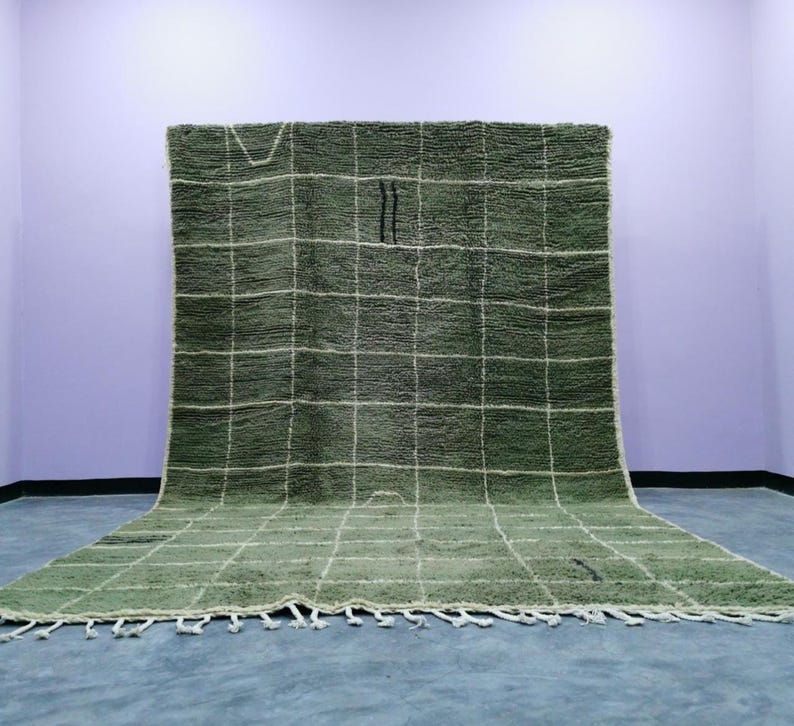 May include: A large, rectangular green rug with a grid pattern of white lines. The rug has a thick, textured pile and a fringe along the bottom edge. Two black vertical lines are near the center of the rug.