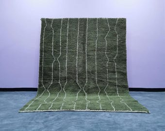 May include: A green rug with white vertical lines and diamond-shaped patterns. The rug is made of a thick, textured material and is displayed against a purple wall and blue floor. The rug's design adds a touch of modern style.