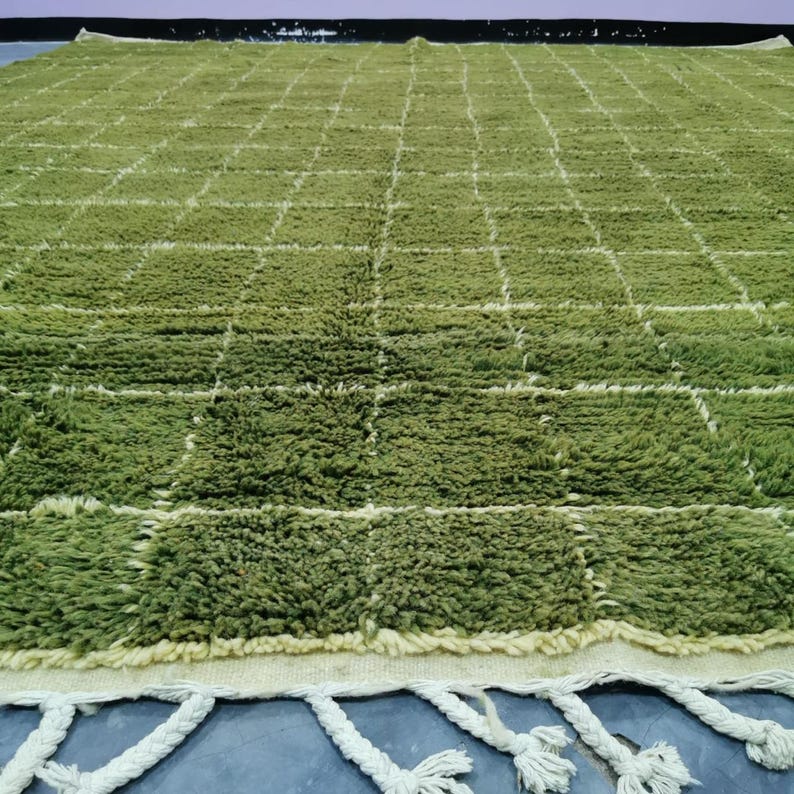May include: A large, rectangular green rug with a grid pattern of white lines. The rug has a shaggy texture and a cream-colored border with white tassels along the edge. The rug is made of a soft, plush material.