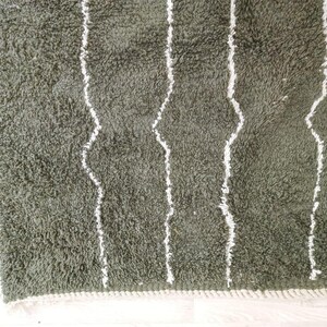 May include: Close-up of a green, shaggy rug with white, vertical, wavy stripes. The rug has a soft, textured appearance and a white border along the edge. The rug is likely made of a plush material.