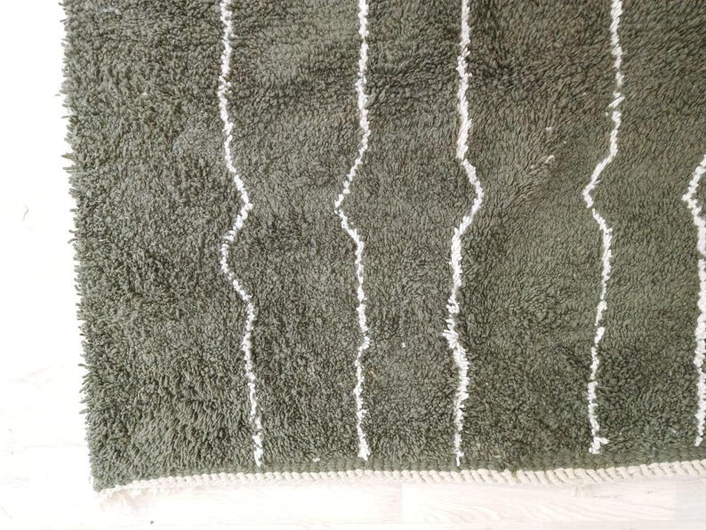 May include: Close-up of a green, shaggy rug with white, vertical, wavy stripes. The rug has a soft, textured appearance and a white border along the edge. The rug is likely made of a plush material.