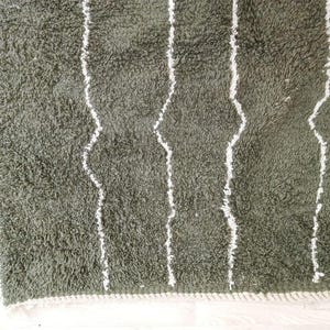 May include: Close-up of a green, shaggy rug with white, vertical, wavy stripes. The rug has a soft, textured appearance and a white border along the edge. The rug is likely made of a plush material.