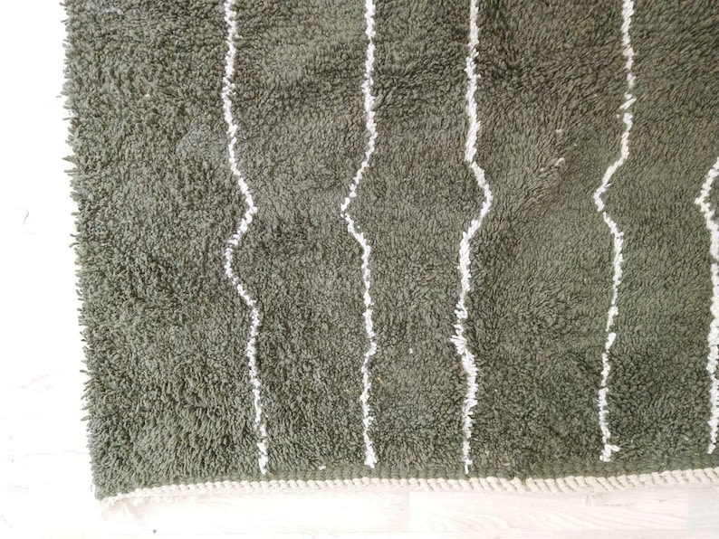 May include: Close-up of a green, shaggy rug with white, vertical, wavy stripes. The rug has a soft, textured appearance and a white border along the edge. The rug is likely made of a plush material.