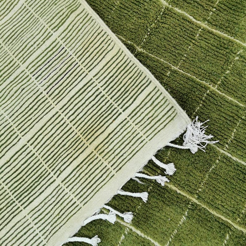 May include: Overhead shot of two rugs. One rug is a light green with dark green stripes, and the other is a darker green with a grid pattern. The light green rug has white tassels on the edge.